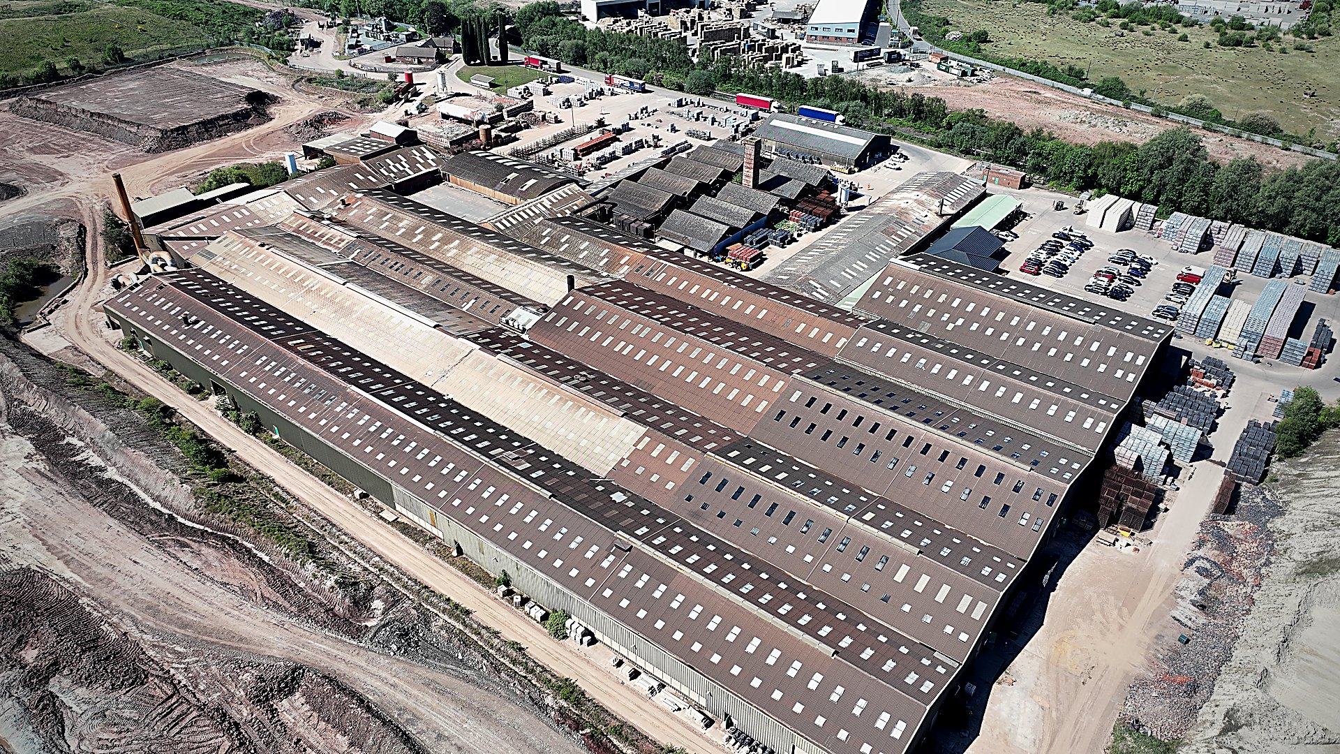 Aerial reconnaissance over a multi-building industrial portfolio: long parallel-shed roofs surveyed by Solar Surveys for commercial PV pre-construction structural assessment, captured during an engineering condition survey.