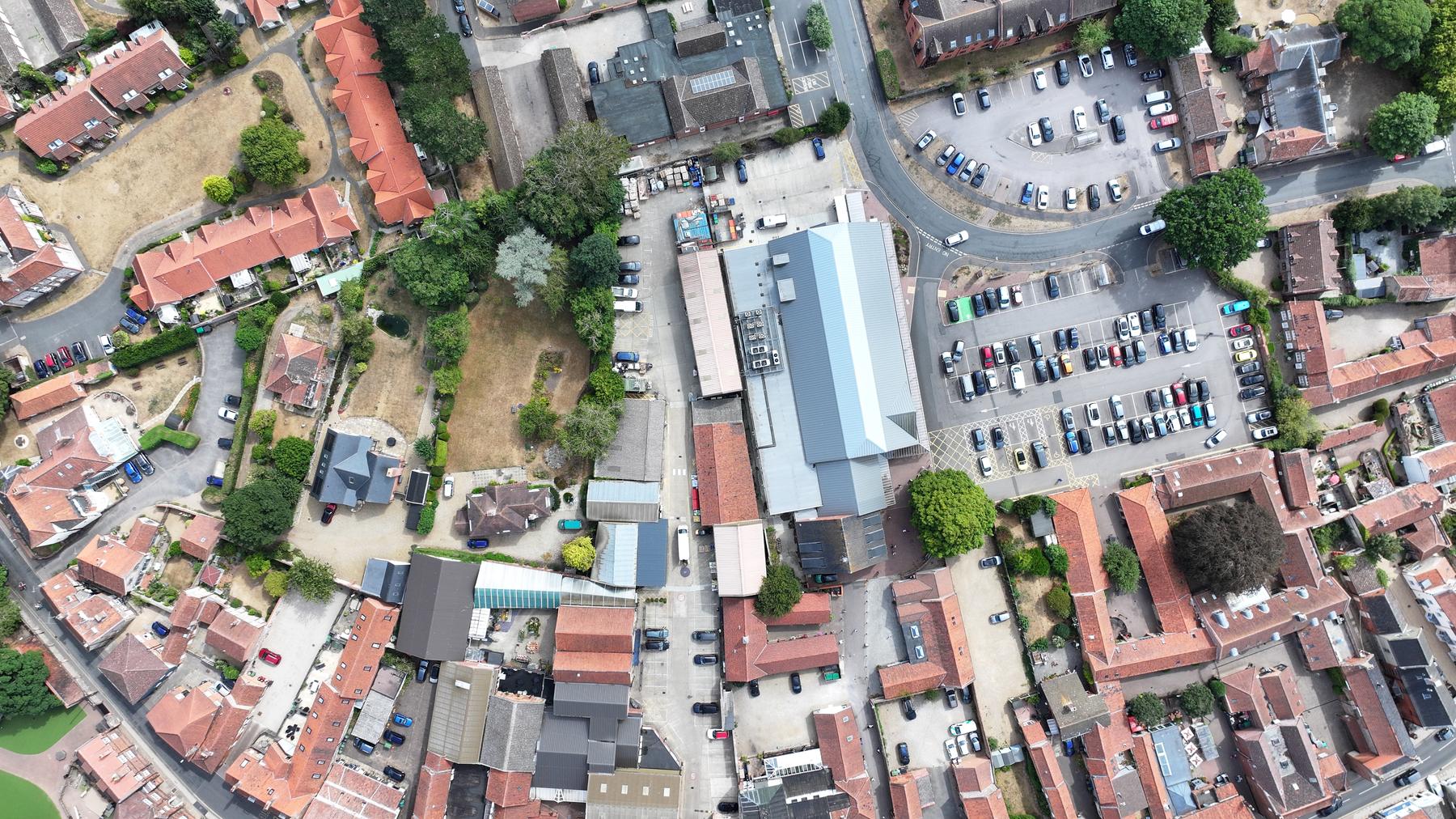 Wide overhead drone view of a market-town centre site with clay pantile, sheet and flat roofs
