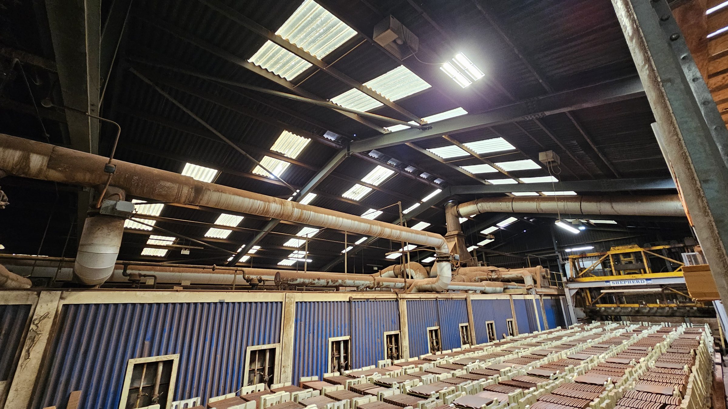On-site structural survey: ridge beam and purlin spacing assessment with roof skylight grid visible above industrial production hall