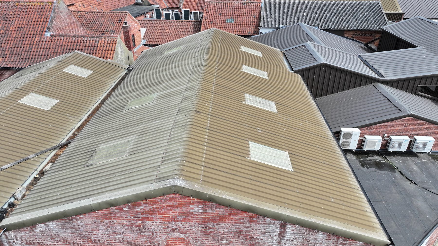 Aerial view of an ageing corrugated sheet roof with translucent rooflight panels, set among a town roofscape, recorded during a structural survey